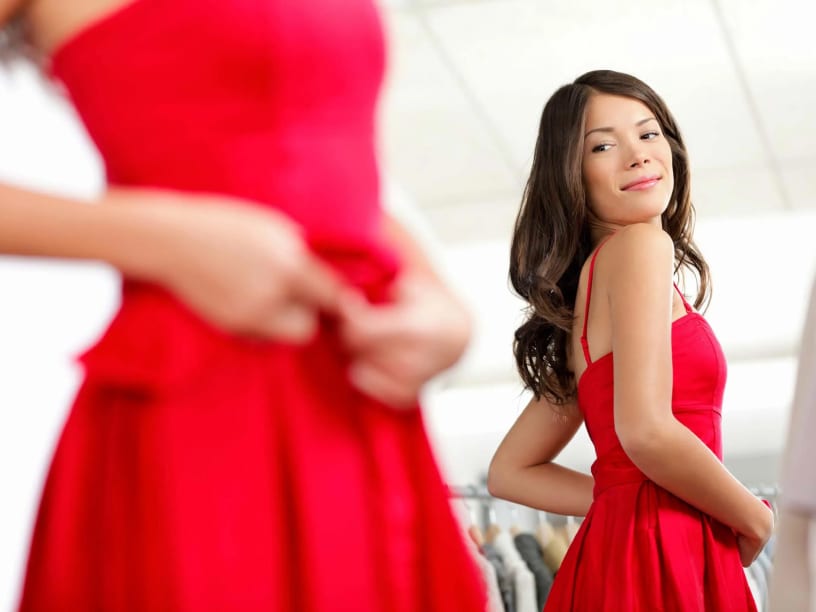 Mulher em vestido vermelho observa seu reflexo no espelho, expressando elegância e autoconfiança.